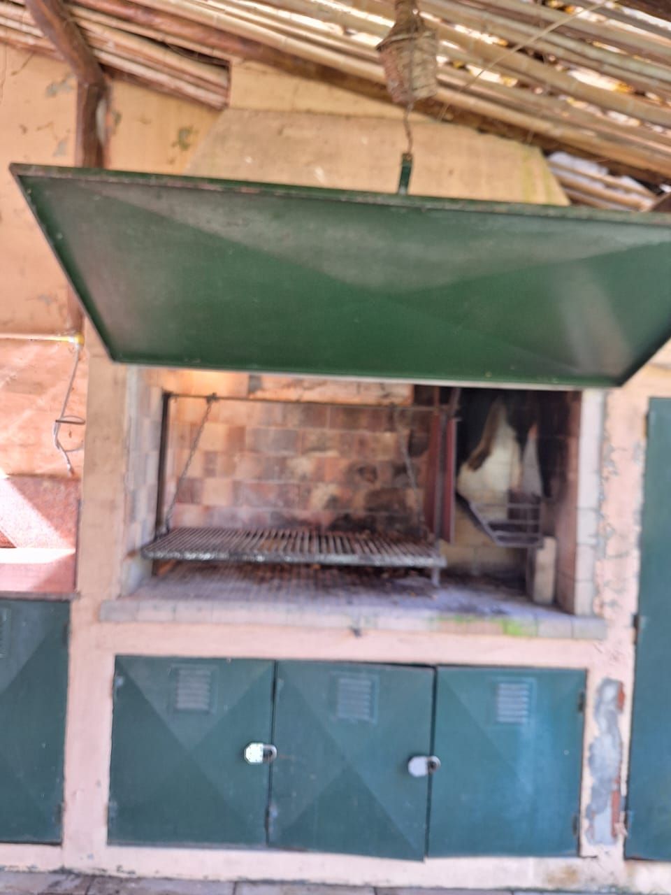 Barbacoa exterior de ladrillo con campana, parrilla y puertas de metal verde.