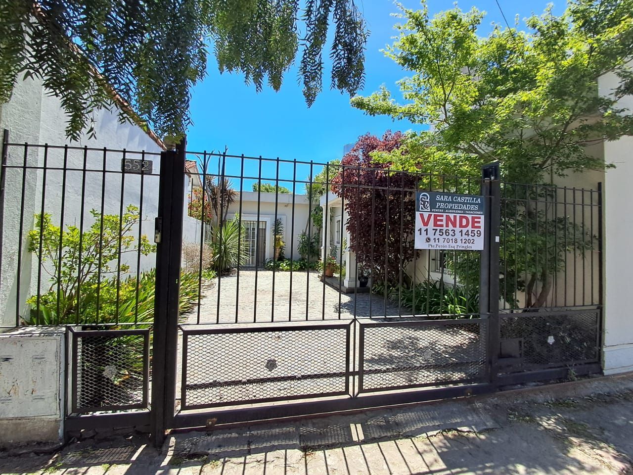 Una casa en venta tras una verja negra, un cartel de