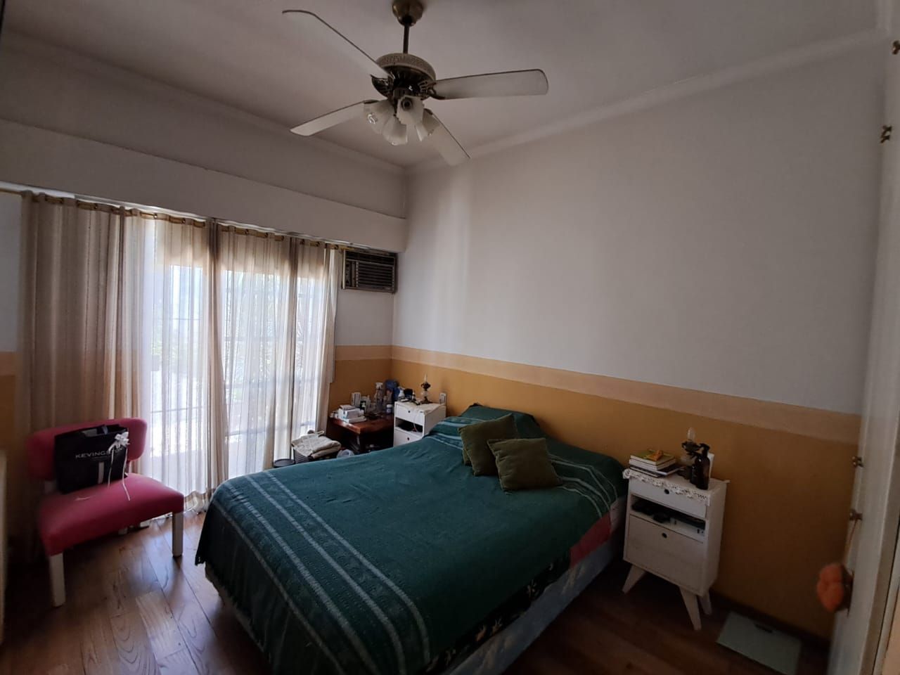 Dormitorio con cama, mesitas de noche y ventana con cortinas; suelo de madera; paredes blancas y amarillas.