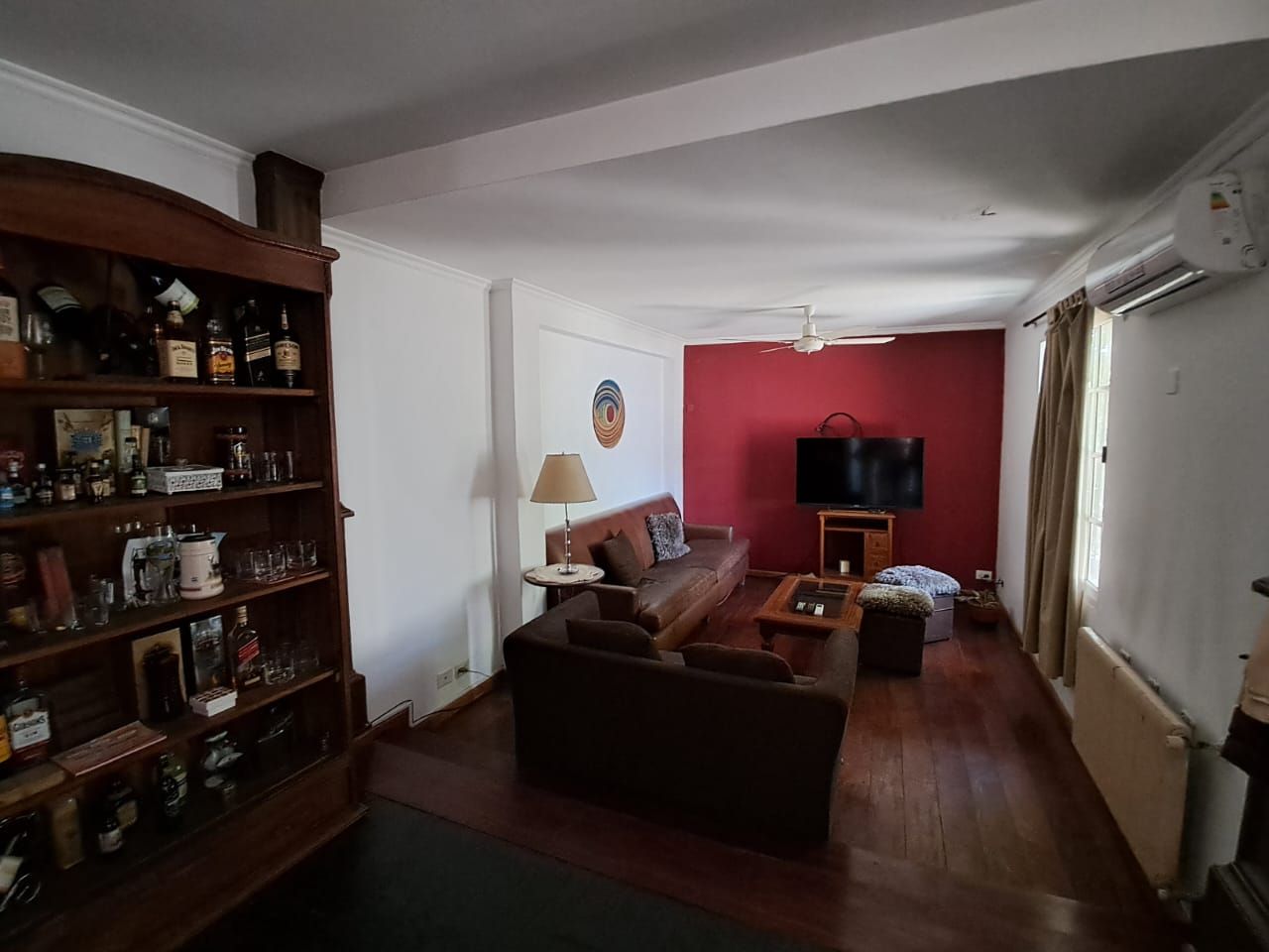 Salón con suelo de madera, sofás de cuero marrón, pared decorativa roja y una gran estantería.