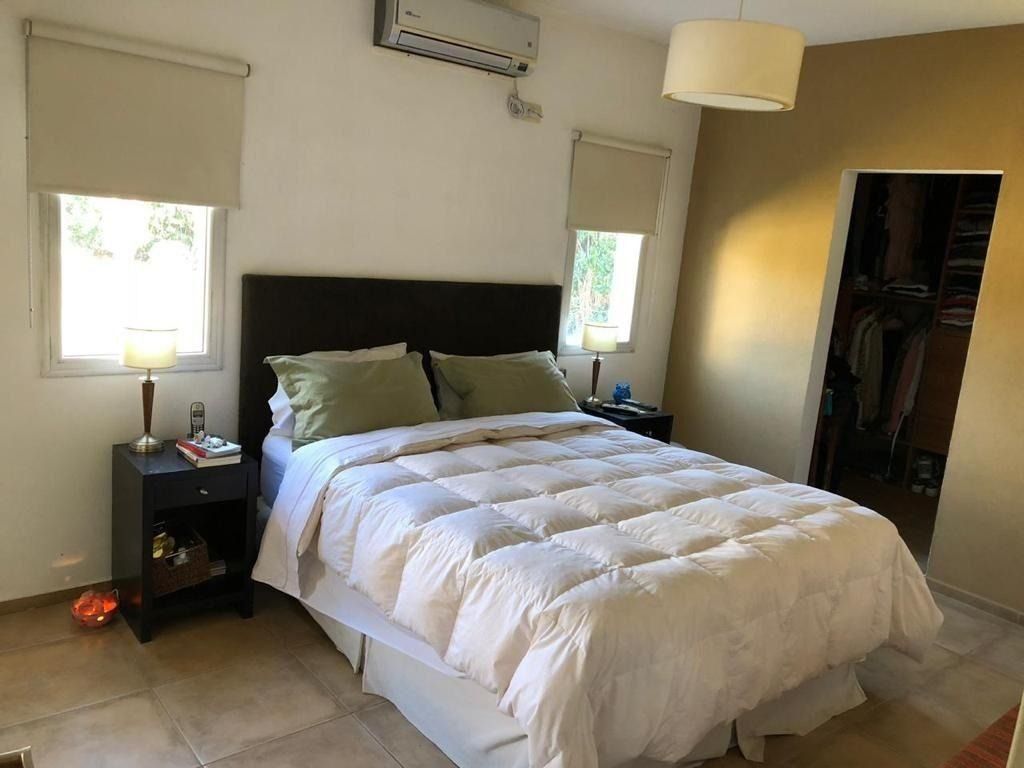 Dormitorio con cama, mesitas de noche, ventanas y armario; colores neutros.