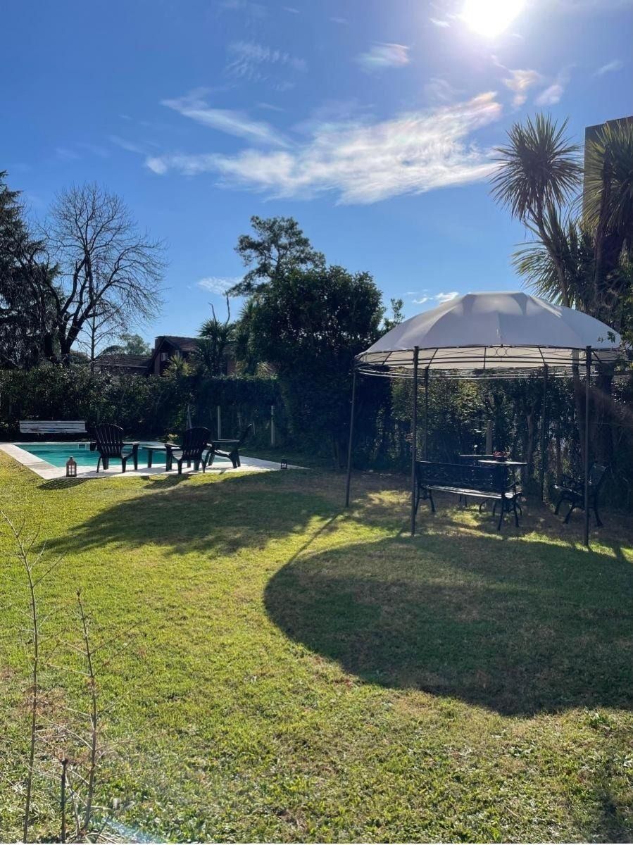 Jardín con cenador, piscina y árboles bajo un cielo azul soleado.