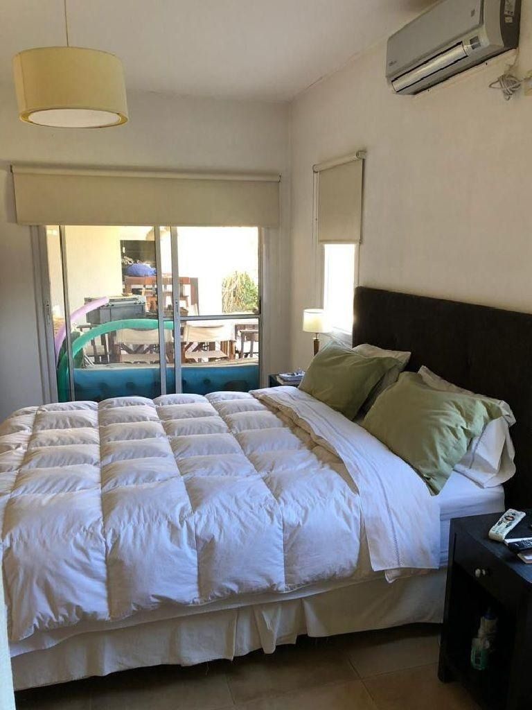 Dormitorio con cama, balcón con vistas y aire acondicionado. Ropa de cama blanca, almohadas verdes y cabecero oscuro.