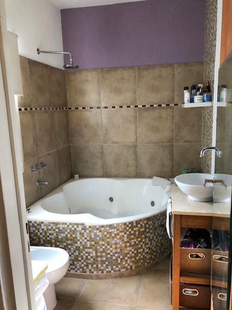 Baño con jacuzzi esquinero, azulejos beige, frontal de mosaico, lavabo blanco, tocador de madera