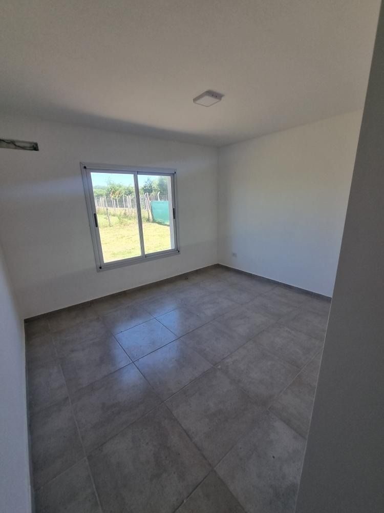 Habitación vacía con suelo de baldosas grises, paredes blancas y una ventana con vistas a la vegetación.