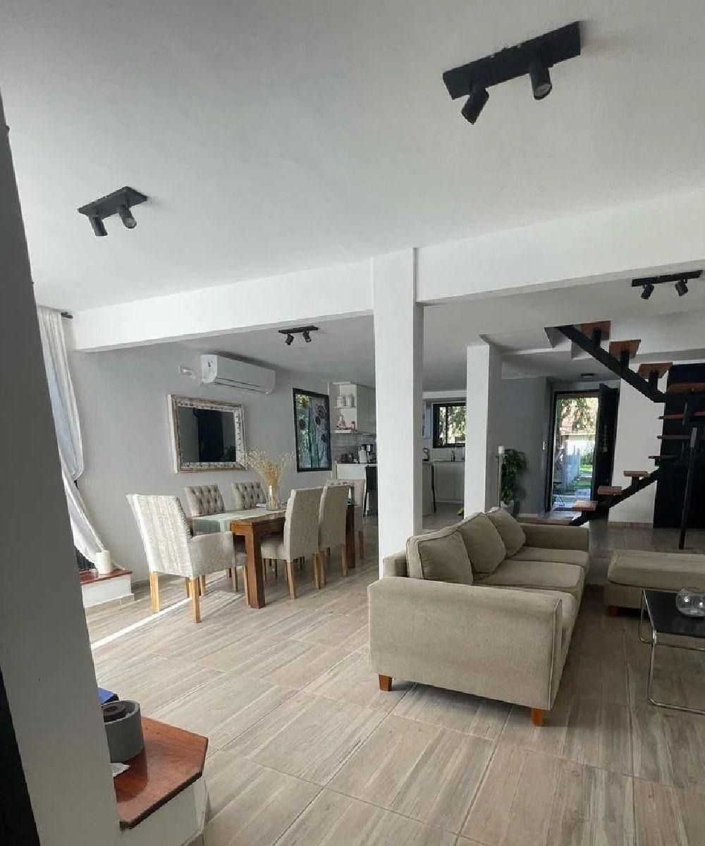 Espacio diáfano con comedor, sofá y escalera. Cuenta con suelo de madera clara e iluminación empotrada.