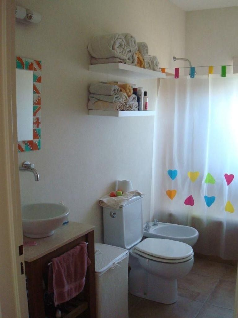Baño con paredes blancas, estantes con toallas, lavabo, inodoro, bidé y coloridas decoraciones en forma de corazón.