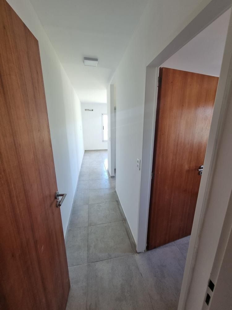 Pasillo estrecho con puertas de madera y suelo de baldosas grises.