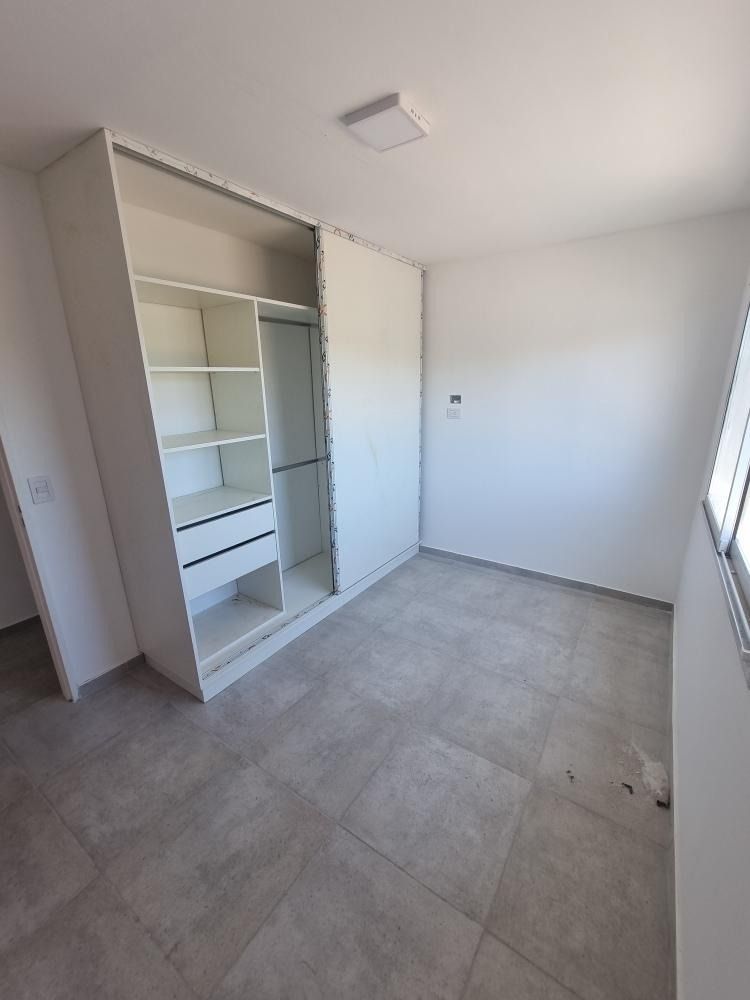 Habitación vacía con armario empotrado blanco, suelo de baldosas grises y ventana pequeña.