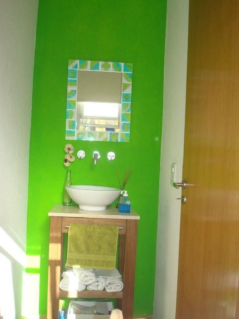 Baño con pared verde brillante, soporte de lavabo de madera, lavabo blanco, espejo y puerta marrón.