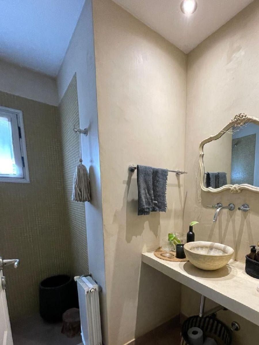 Baño con lavabo color beige, espejo, toallero y una pequeña ventana.