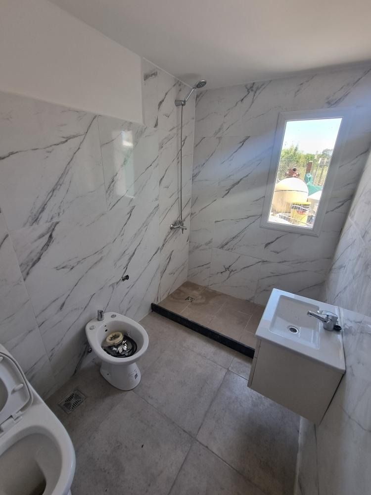 Baño con azulejos blancos imitación mármol, inodoro, bidé, lavabo y ducha.