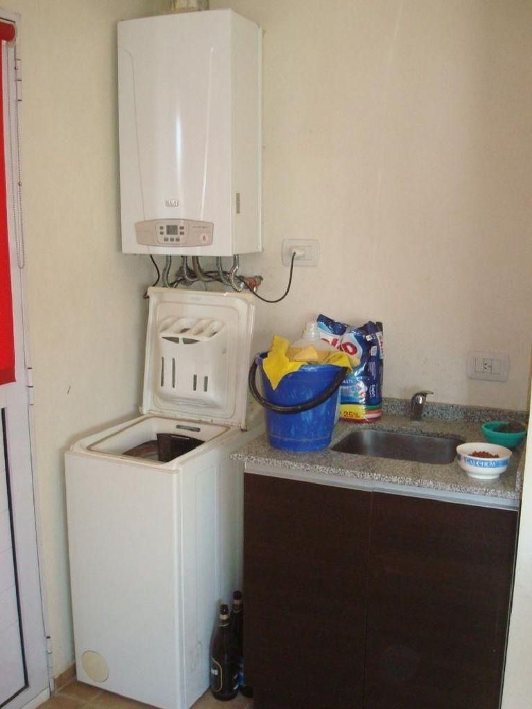 Cuarto de lavandería con lavadora, calentador de agua, fregadero y productos de limpieza.