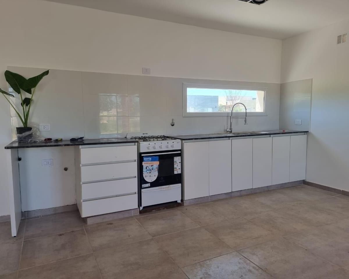 Moderna cocina blanca con armarios, estufa, fregadero y encimera negra, con ventana y suelo de baldosas.