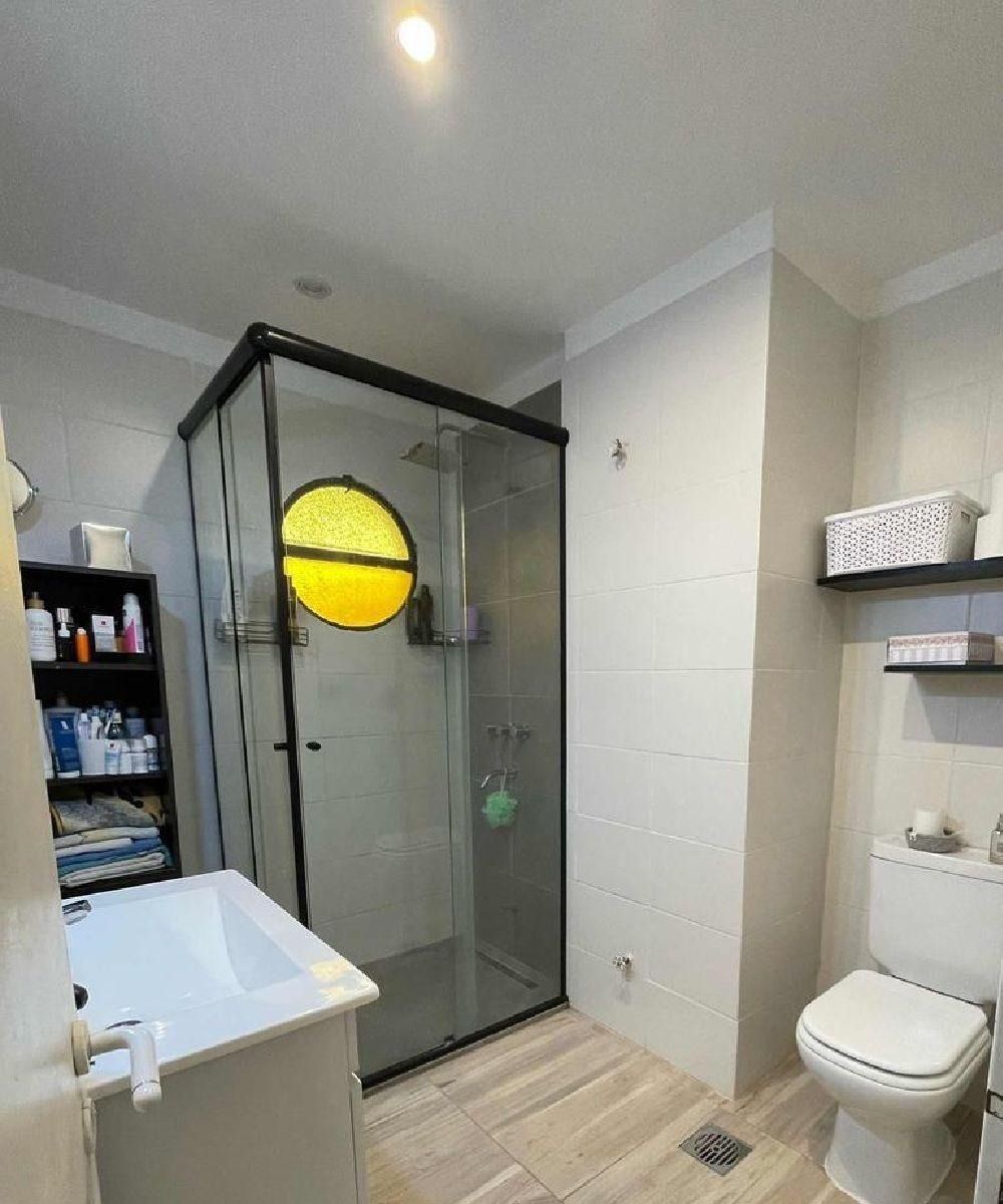 Baño con ducha, inodoro y bañera. La ducha tiene una vidriera circular. Paredes y suelo de color claro.