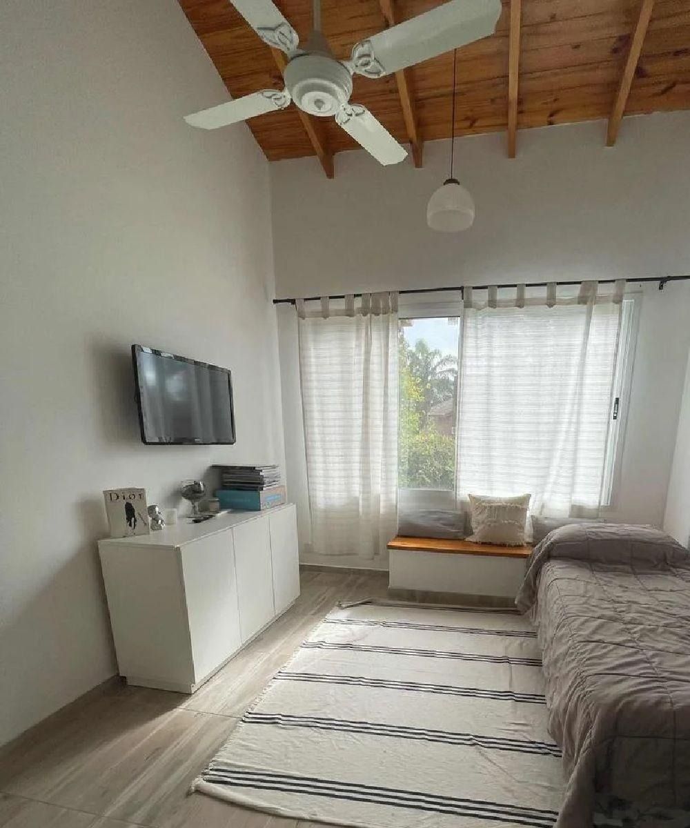 Dormitorio con paredes blancas, techo de madera, televisor, alfombra blanca y cama.