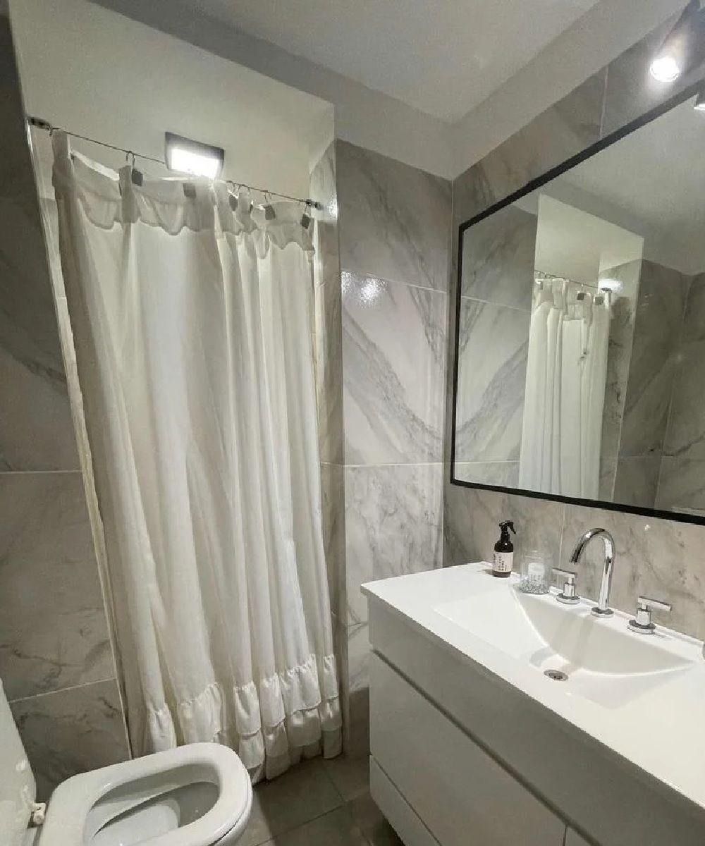 Baño con lavabo, inodoro y cortina de ducha blancos. Espejo grande en la pared.