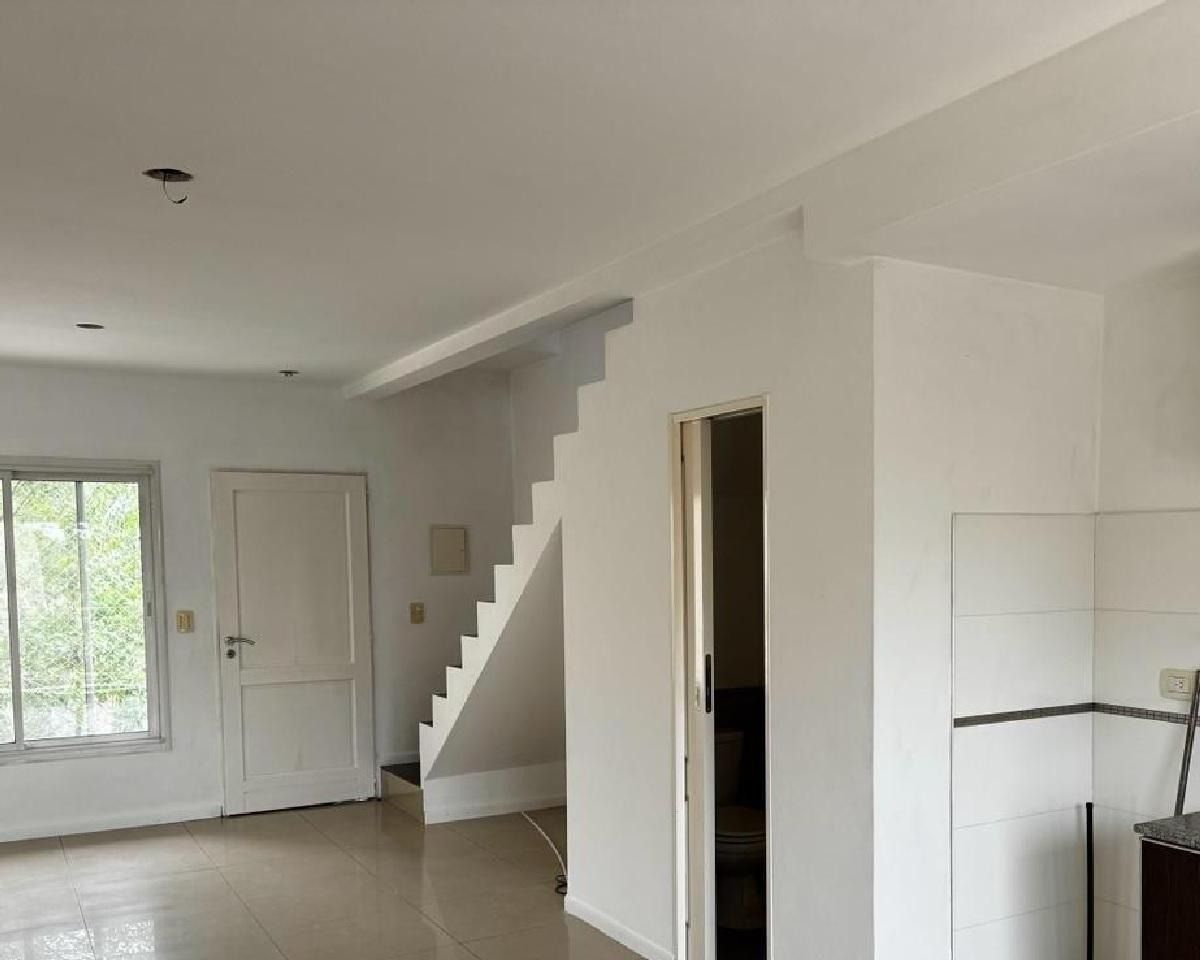 Interior de una habitación pintada de blanco con escaleras, una puerta y una ventana.