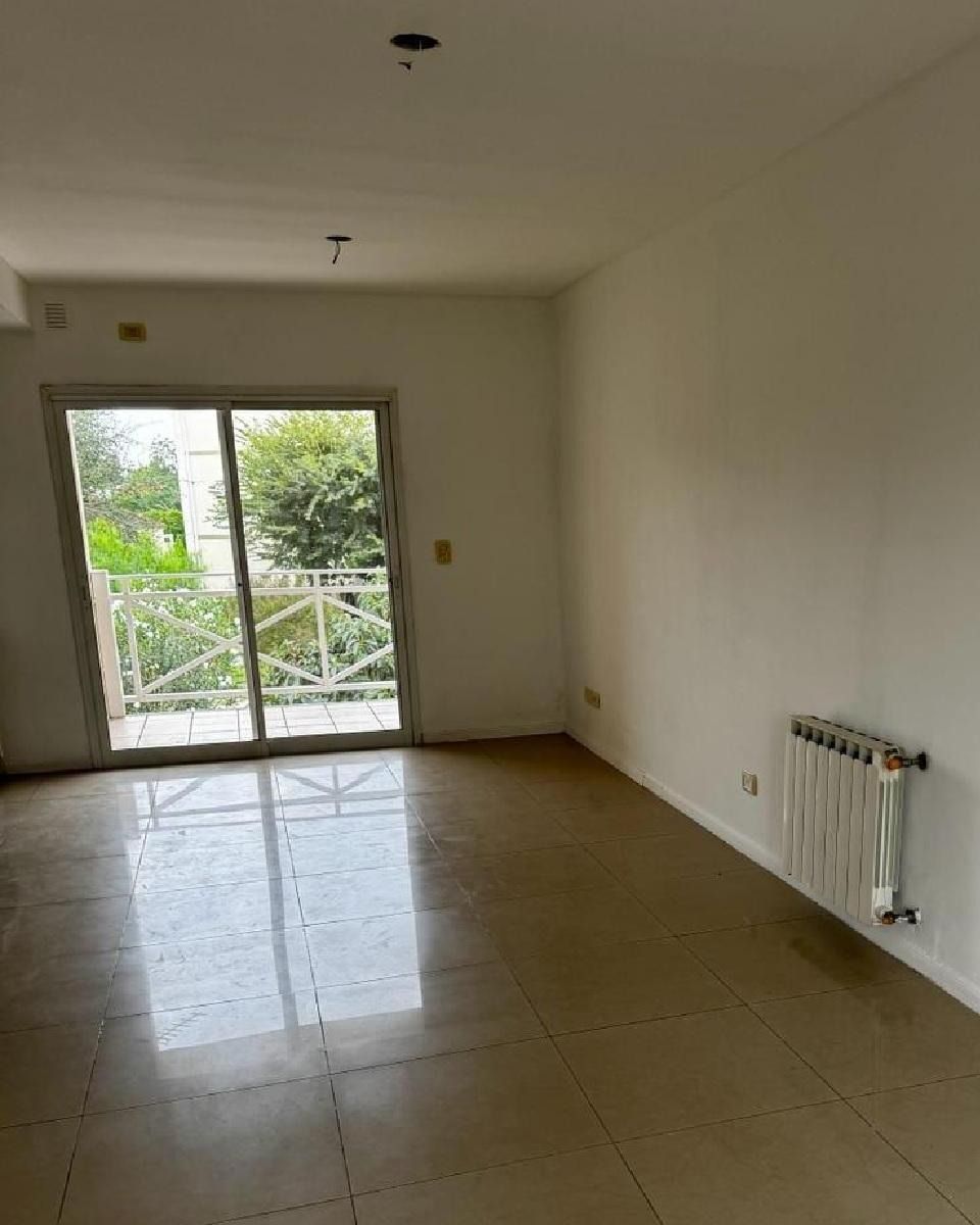 Habitación vacía con suelo de baldosas, radiador y puerta corredera que da a un balcón.