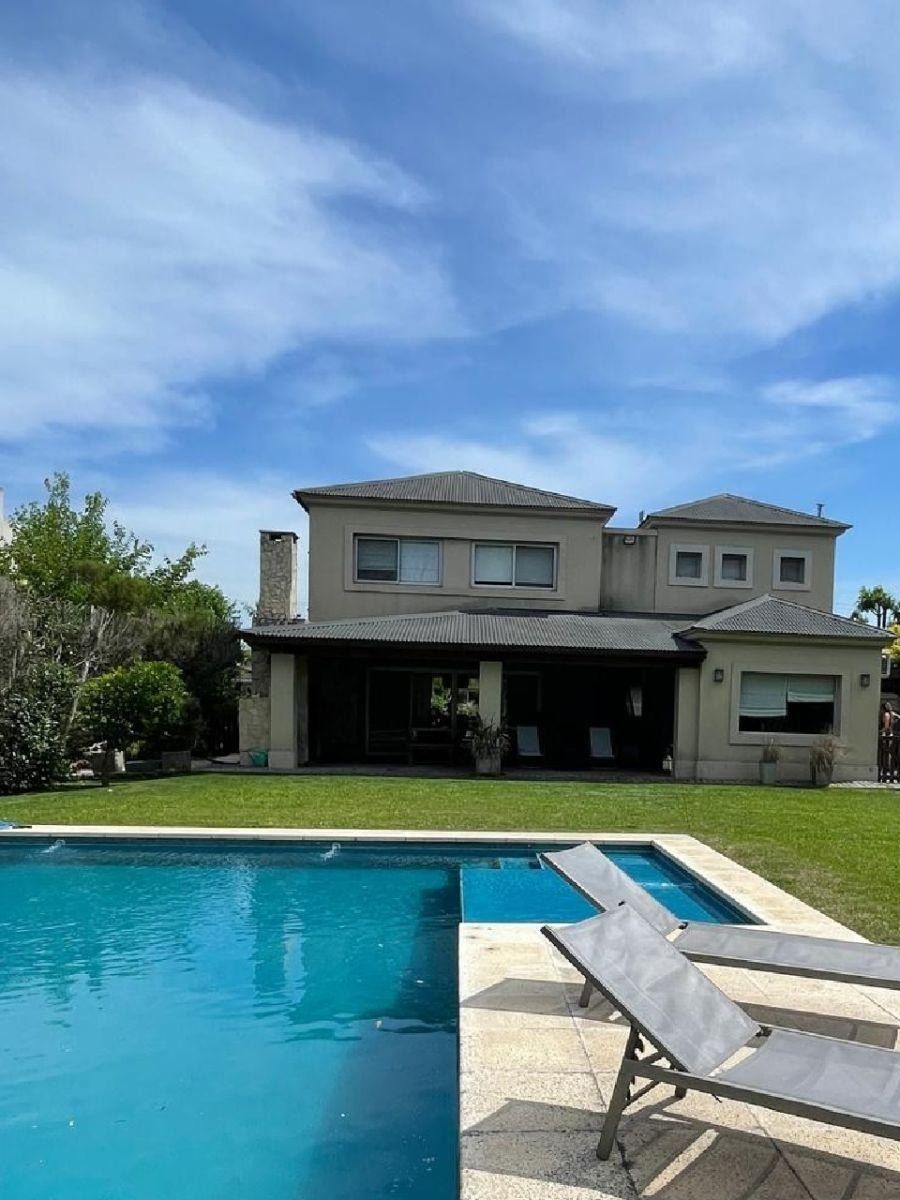 Piscina frente a una casa de dos plantas con césped verde y cielo azul.