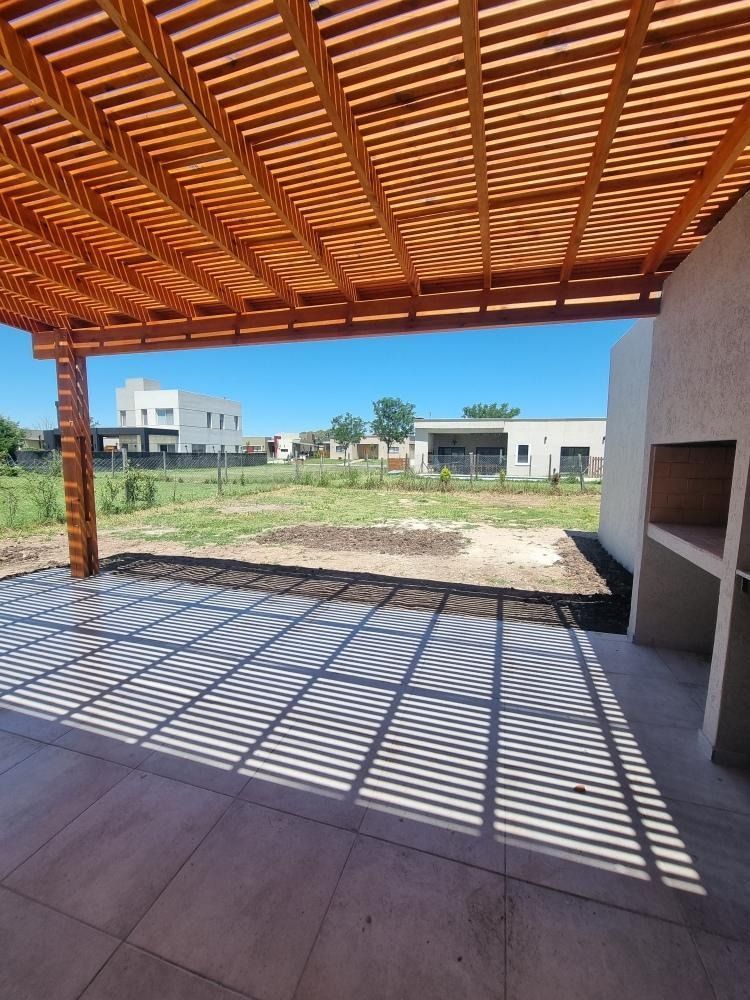 Pérgola de madera que proyecta sombras sobre un patio, con vistas a las casas y una chimenea exterior.