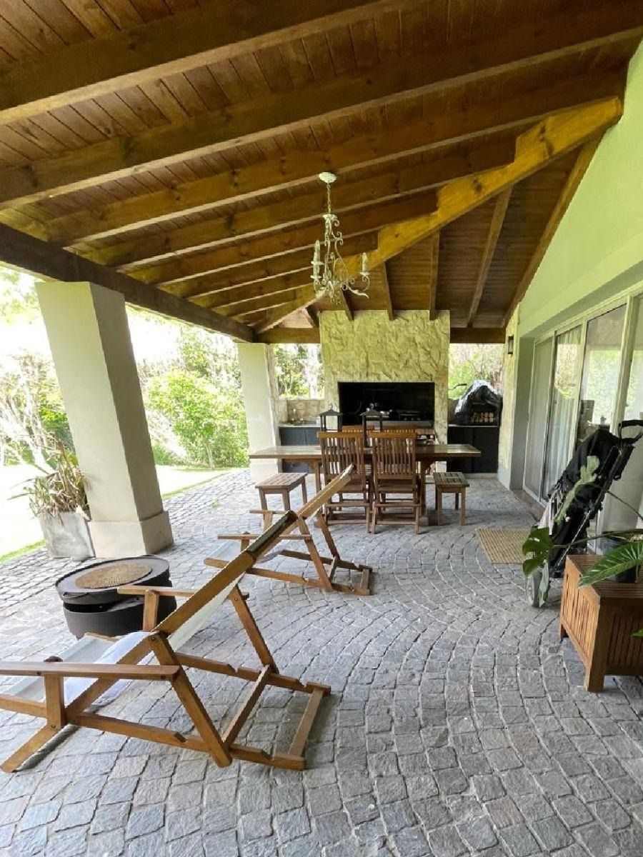 Patio cubierto con muebles de madera, chimenea y suelo de piedra.