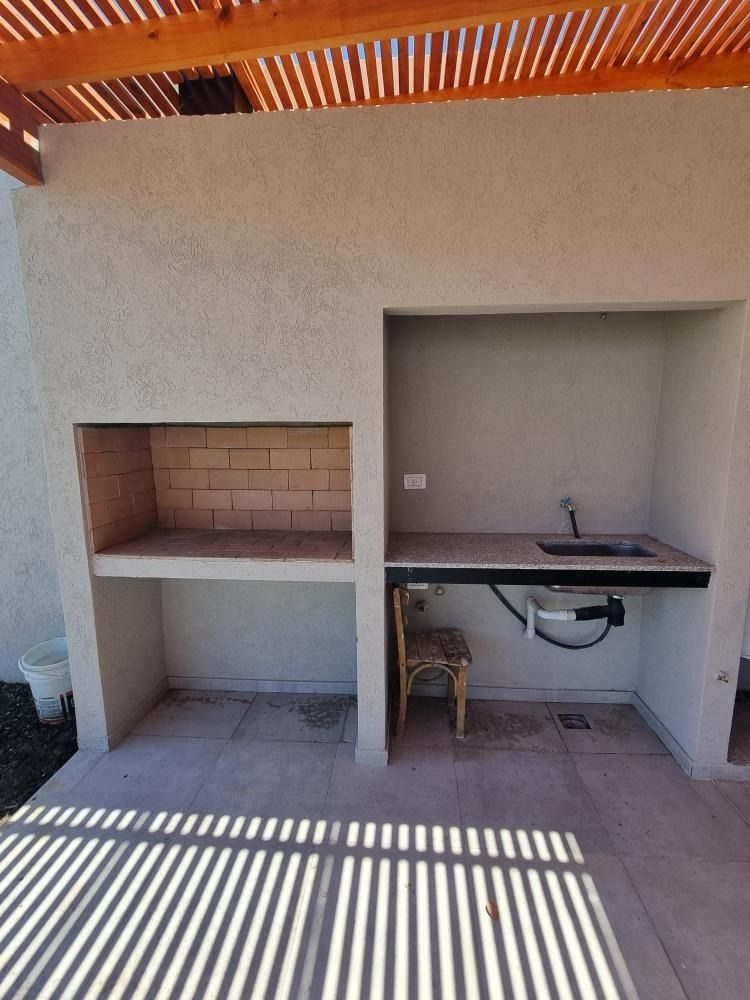 Zona de barbacoa al aire libre con horno de ladrillo, encimera con fregadero y pérgola de madera.