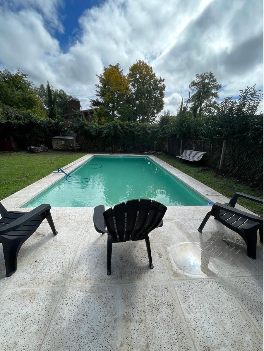 Piscina en un patio trasero con tumbonas en un patio de piedra, bajo un cielo nublado.