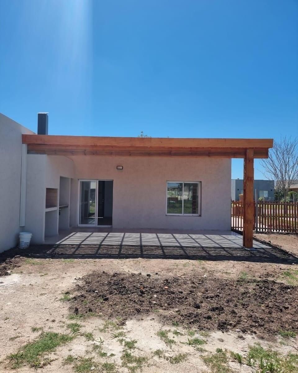 Patio trasero con pérgola de madera, suelo de hormigón, barbacoa empotrada y puerta y ventana exteriores.