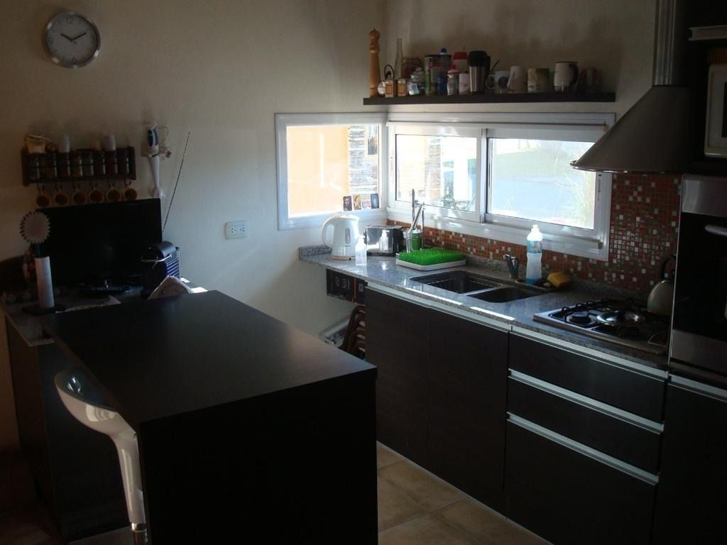 Cocina con armarios oscuros, encimera, ventana e isla con taburete.