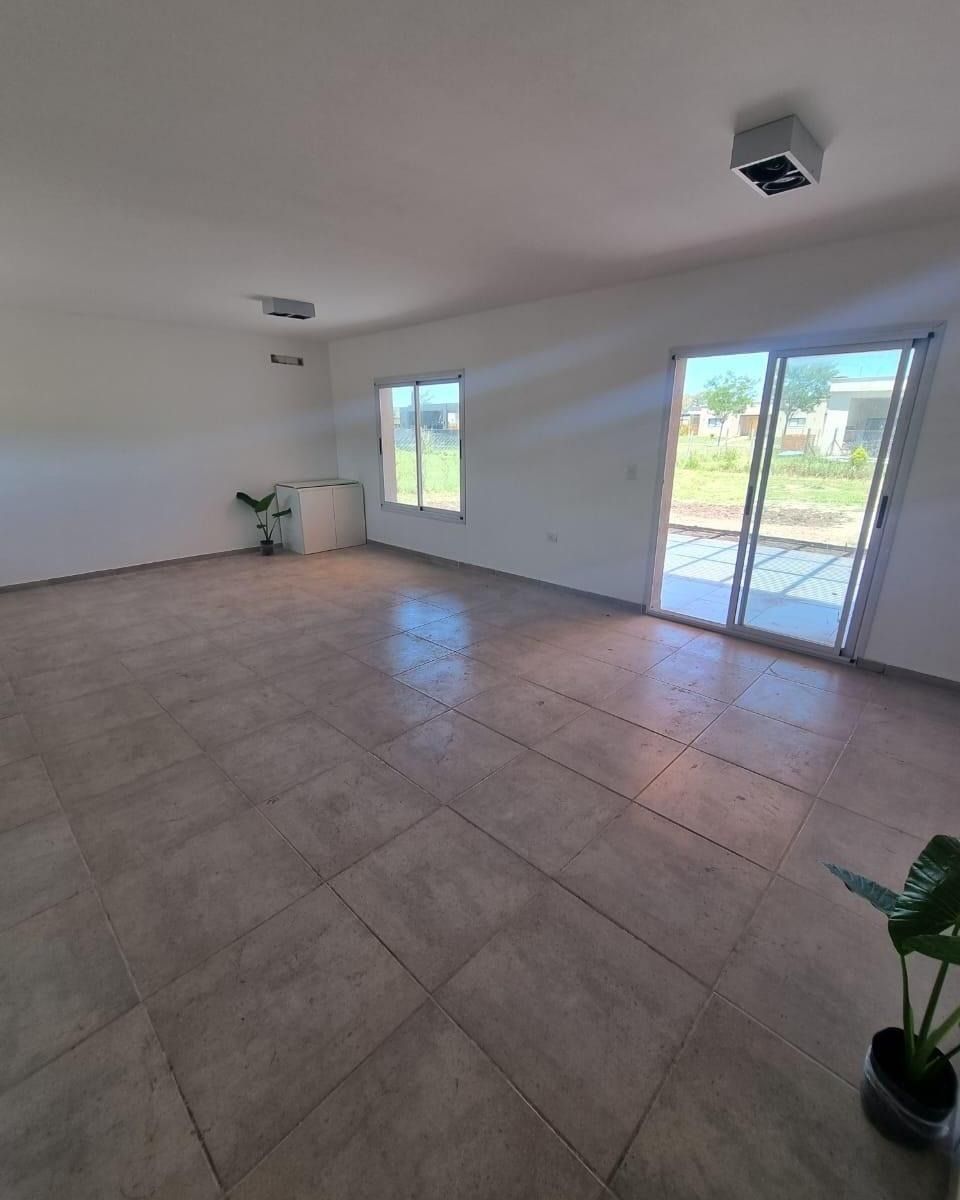 Habitación vacía con suelo de baldosas, paredes blancas, dos ventanas y puerta corredera de cristal que da a un patio.