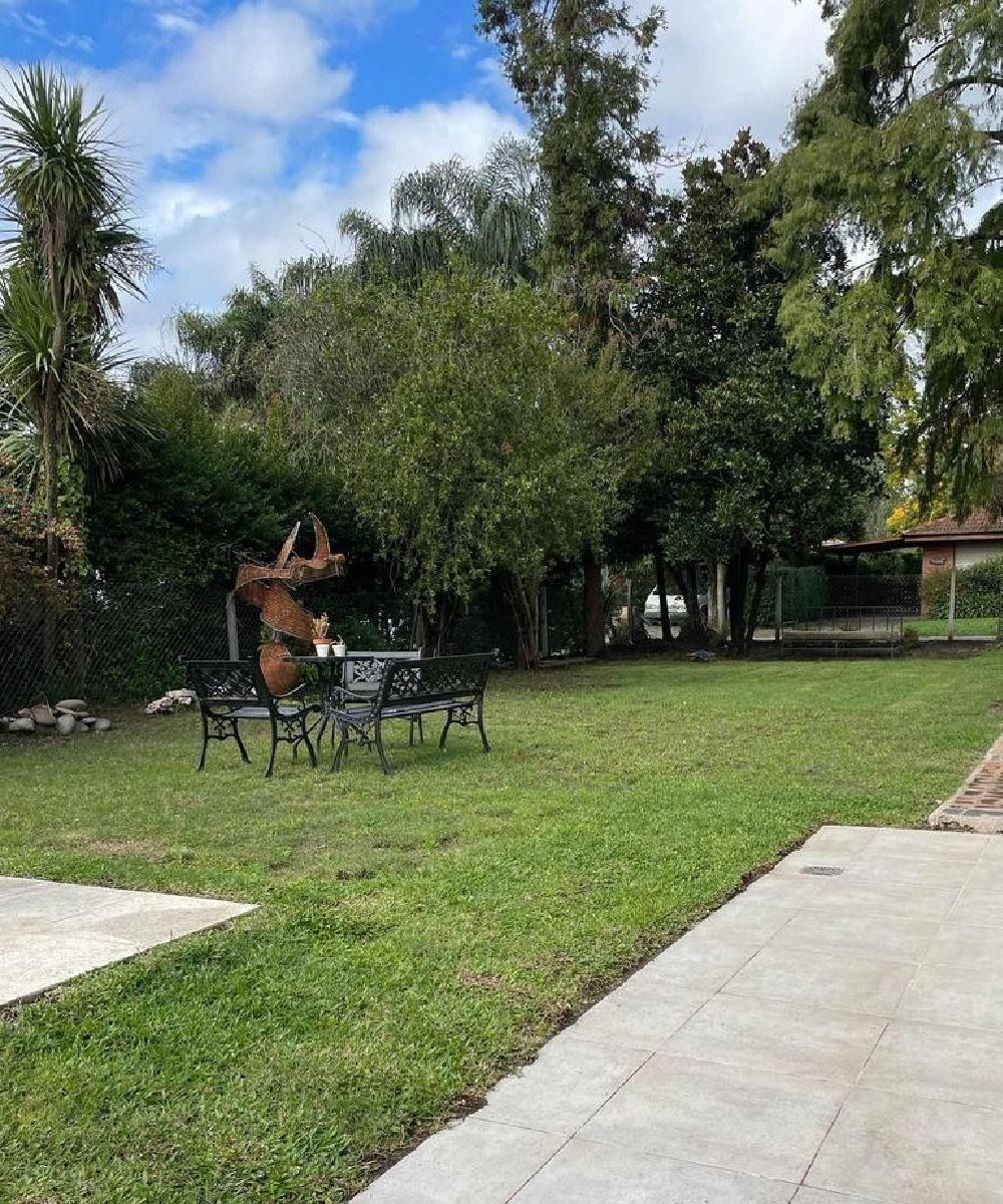 Césped verde con mesa y sillas, rodeado de árboles y un cielo nublado.