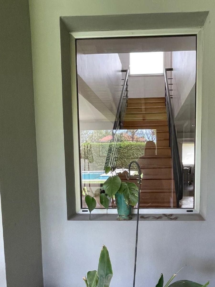 Vista desde la ventana de una escalera, piscina y plantas; interior con paredes grises y marco de ventana de color claro.