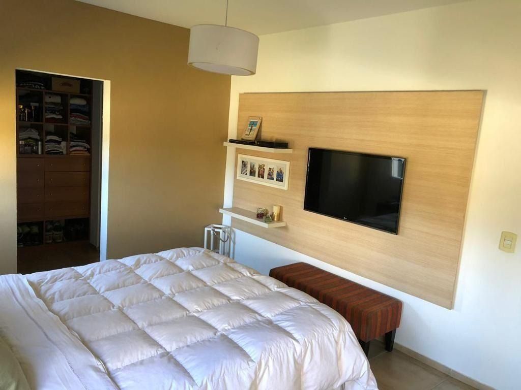 Dormitorio con cama, televisor montado sobre un panel de madera, estantes y un pequeño puf.
