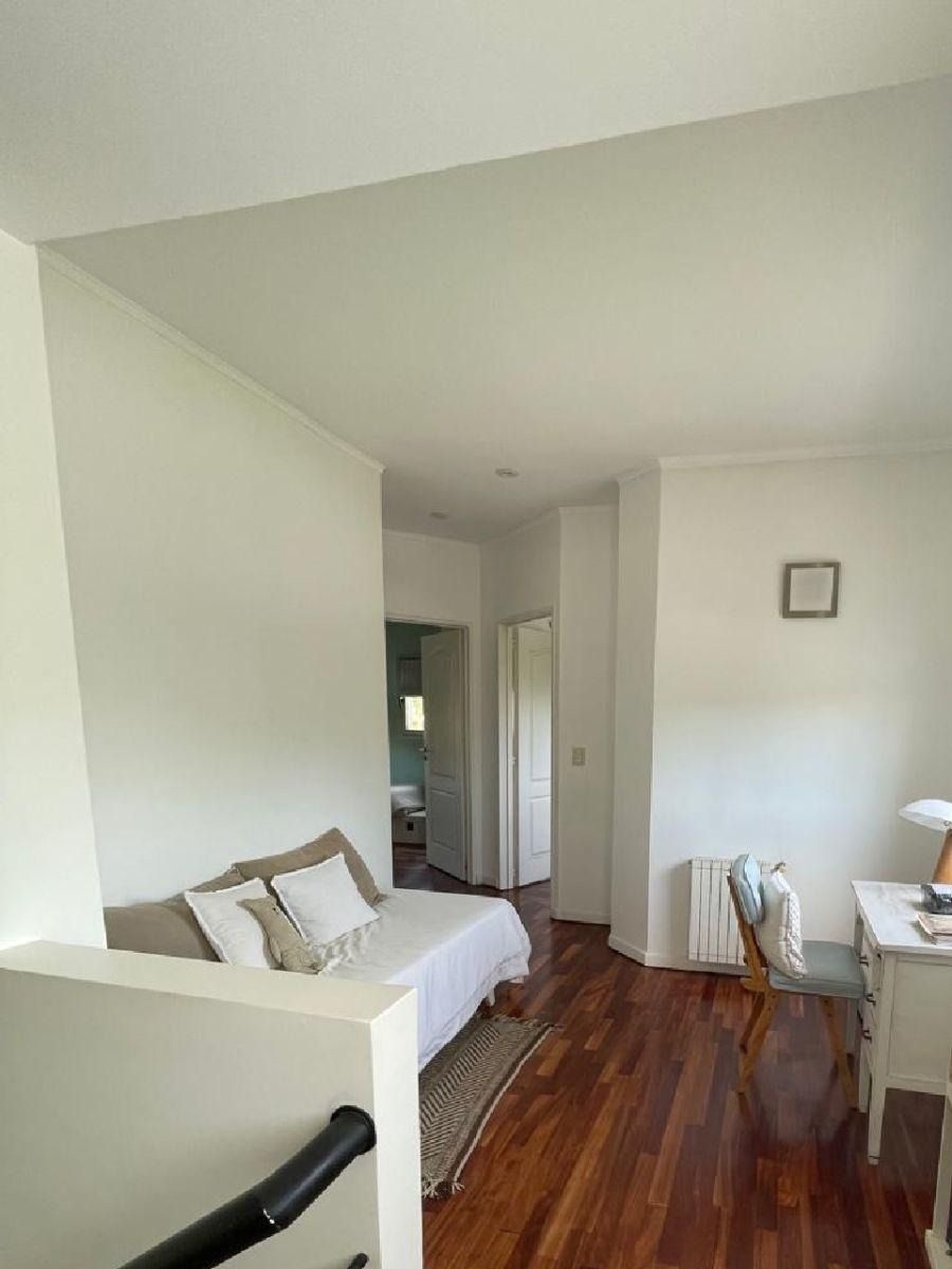 Pasillo con paredes blancas, suelo de madera, sofá cama, escritorio y puerta.