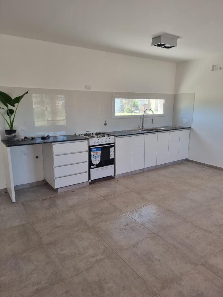 Cocina moderna con gabinetes blancos, encimeras oscuras y estufa de gas. Pisos de baldosas en tonos neutros y salpicadero.