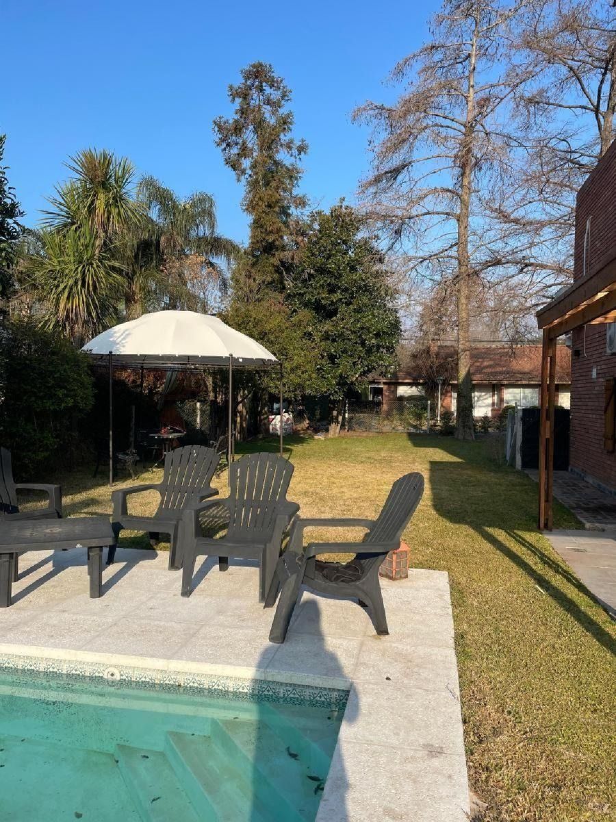 Patio trasero con muebles de exterior, cenador y piscina en un día soleado.