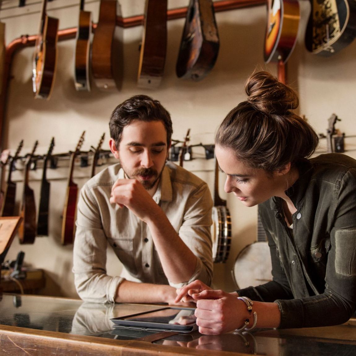 Un uomo e una donna stanno guardando un tablet davanti a un muro di chitarre