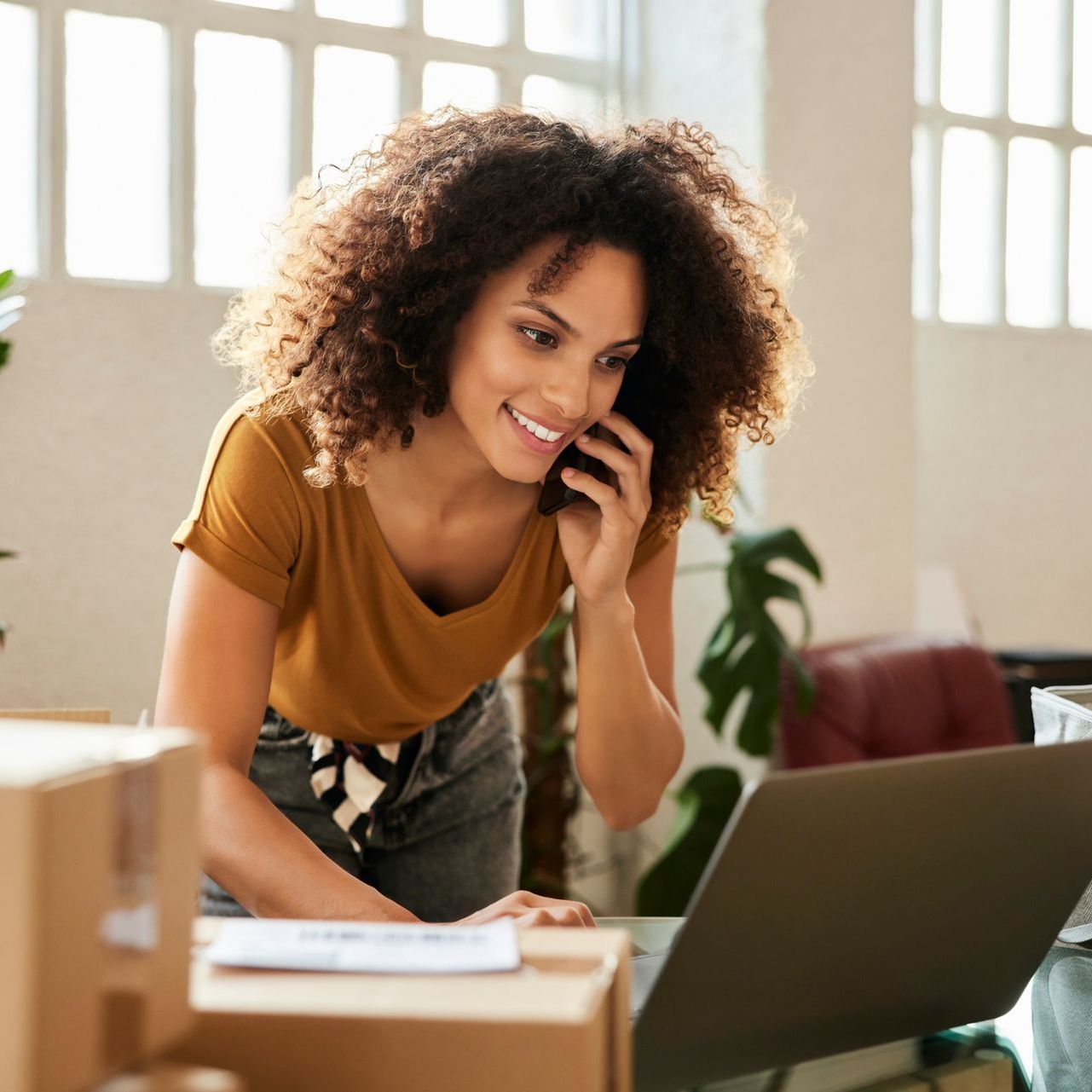 Una donna parla al cellulare mentre utilizza un computer portatile.