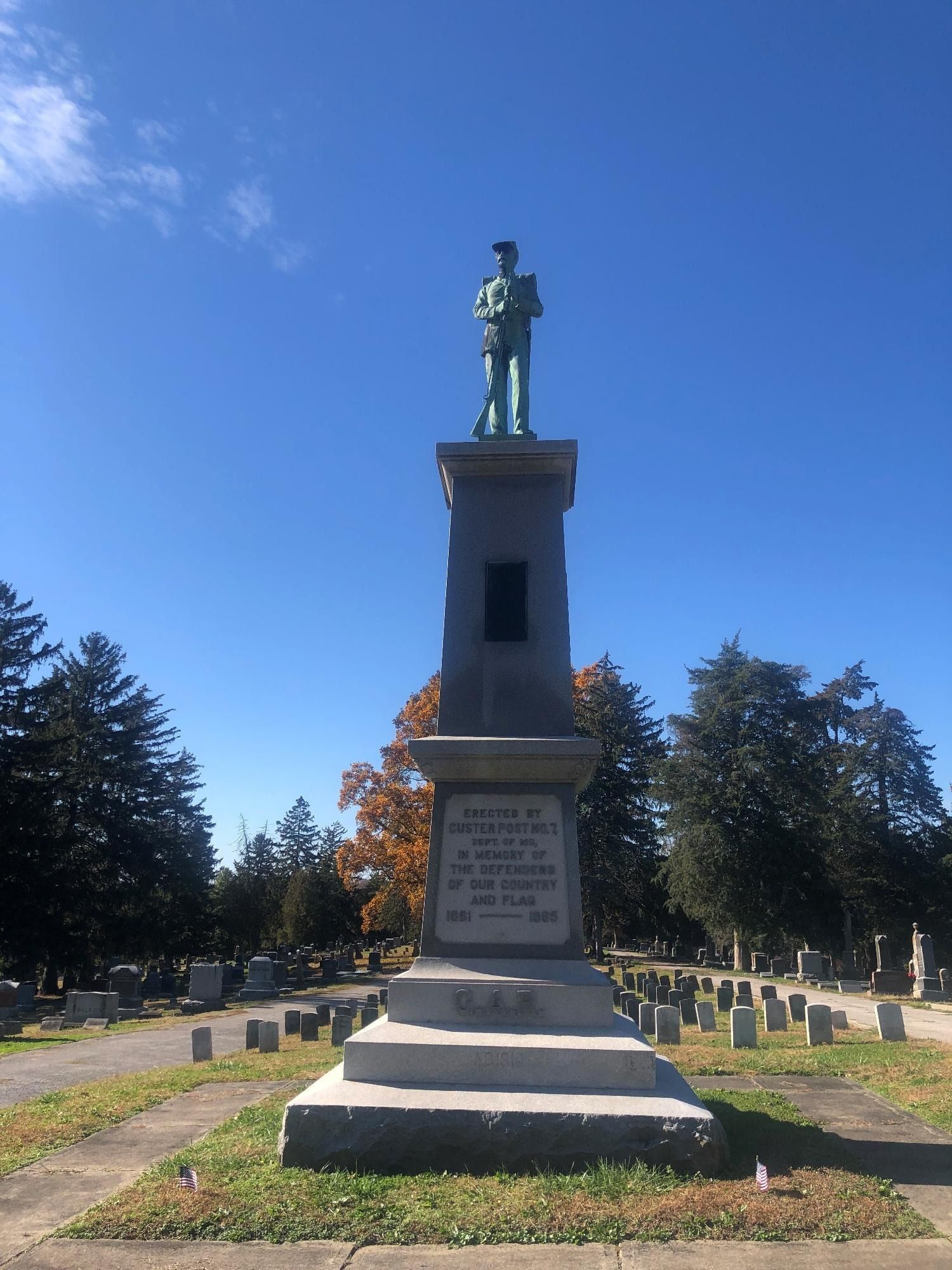 Civil War soldier statue atop a tall column in a cemetery, blue sky.