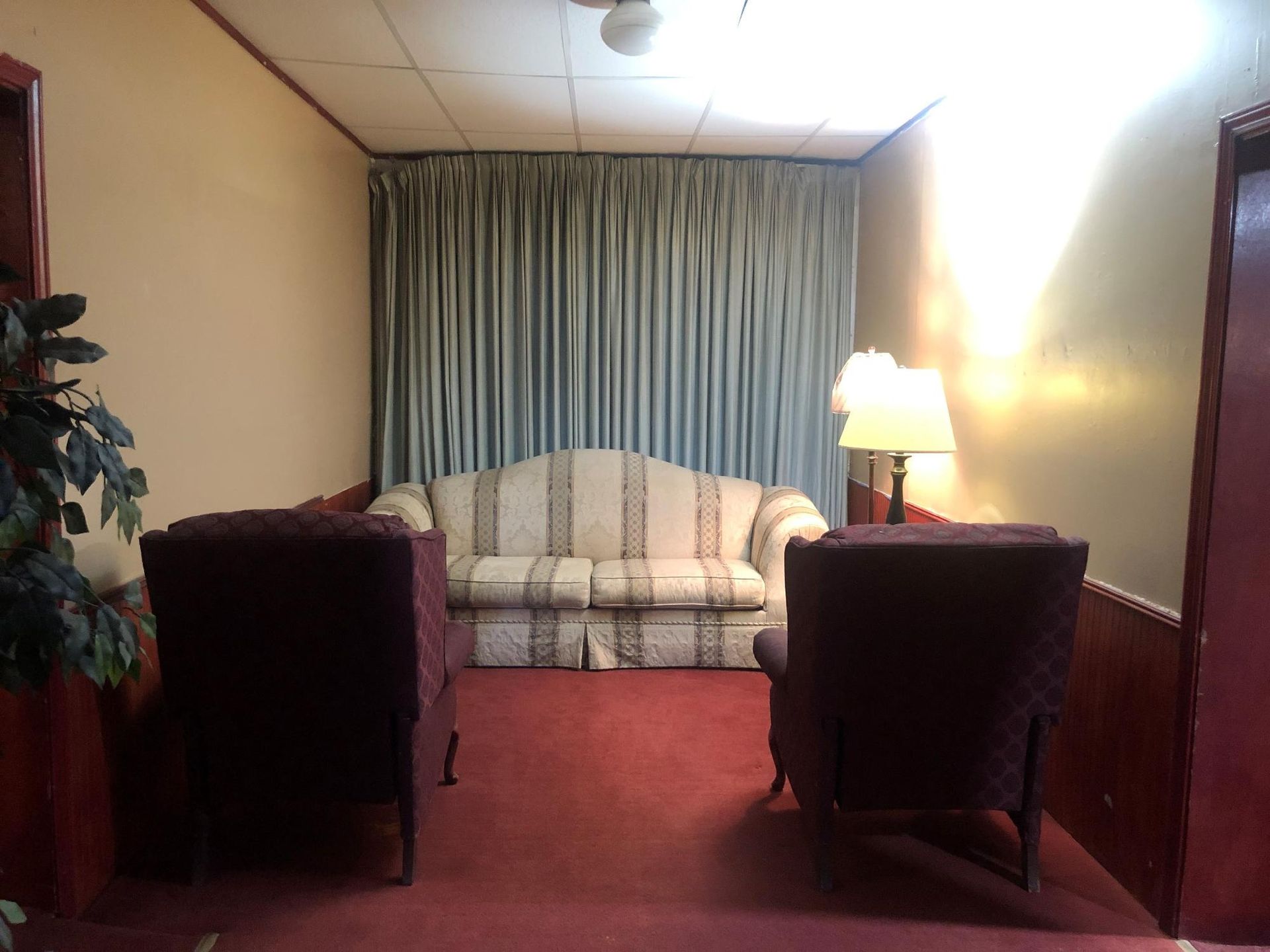 Cozy waiting room with a sofa, two armchairs, a lamp, and curtains against a wall.