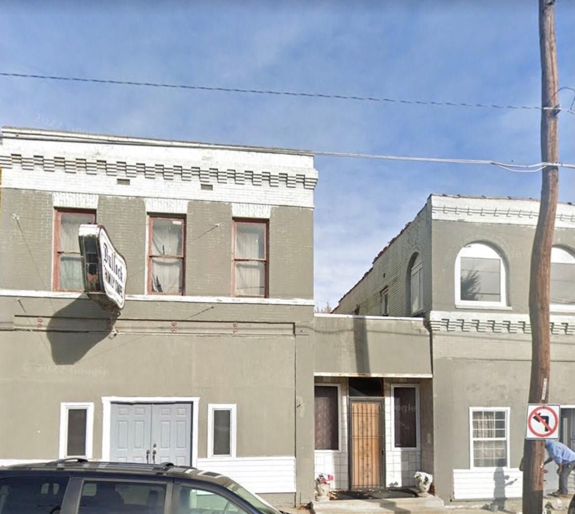 Gray two-story building with white trim; window air conditioner; street sign; blue sky.