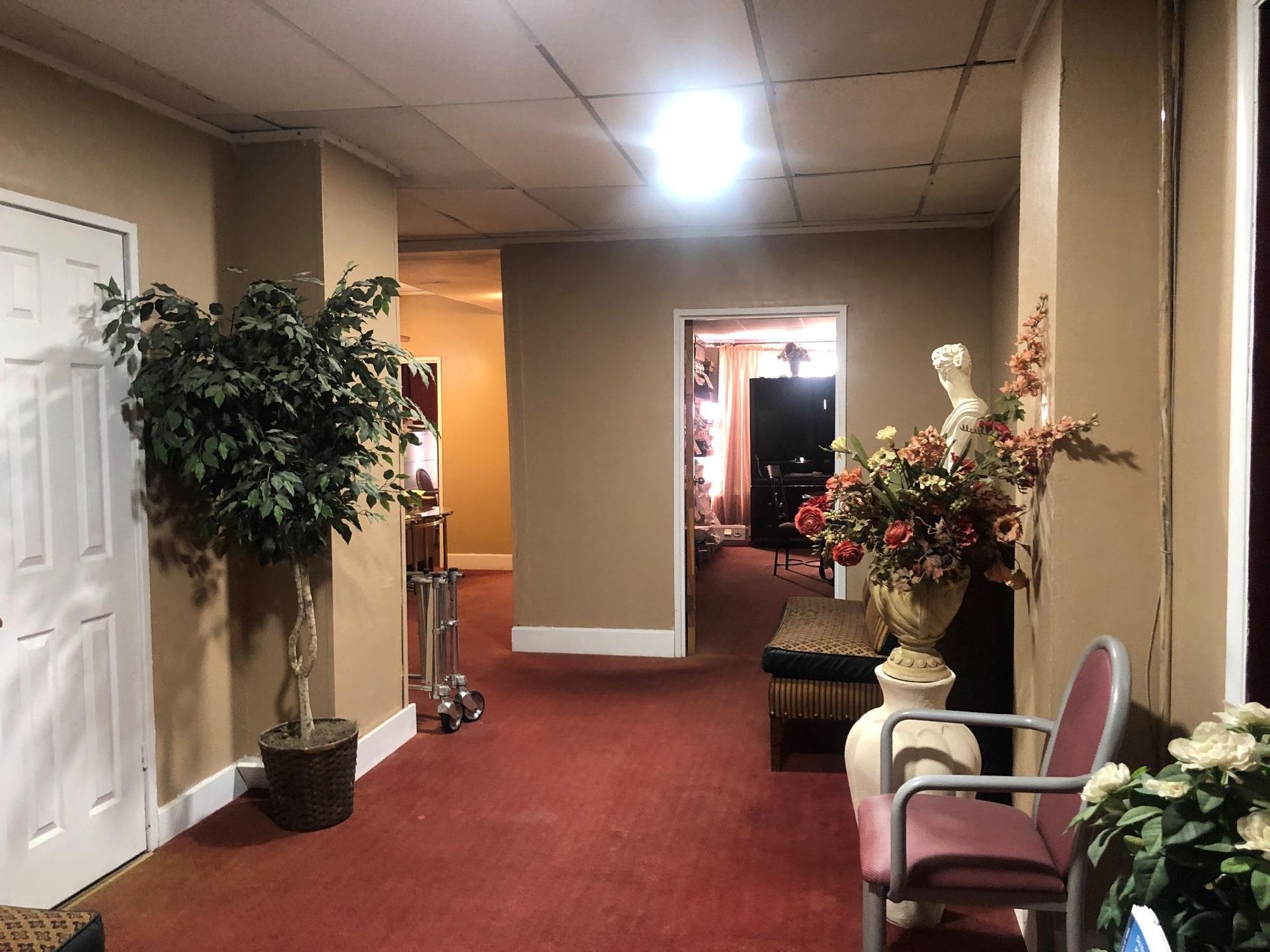 Hallway with red carpet, neutral walls, faux tree, and floral arrangements.