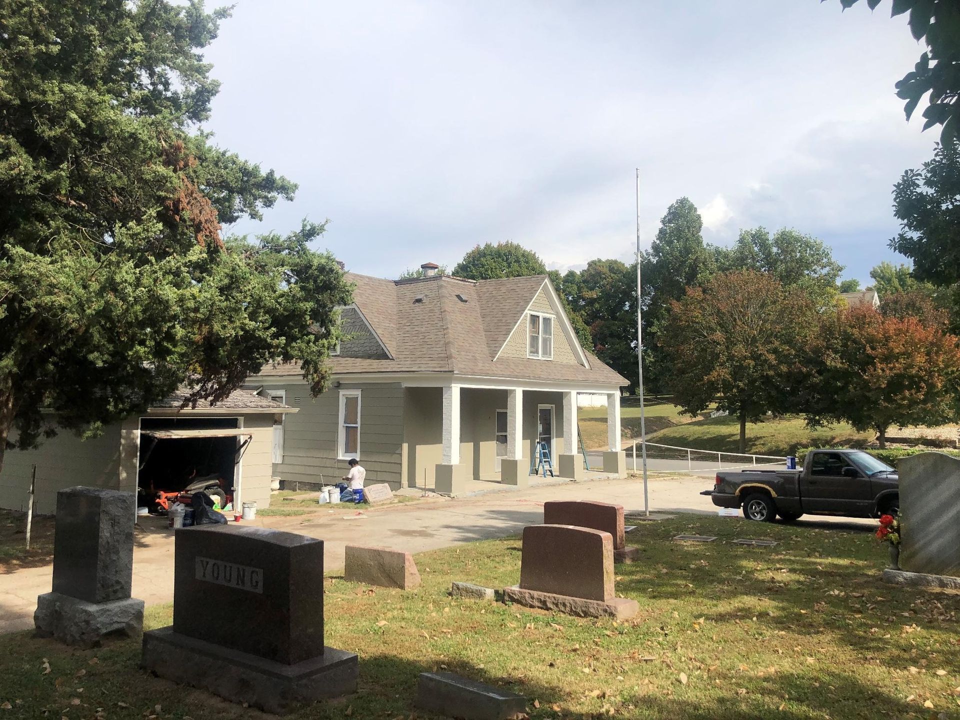 A light green building with a peaked roof, in a cemetery setting, with tombstones in the foreground.