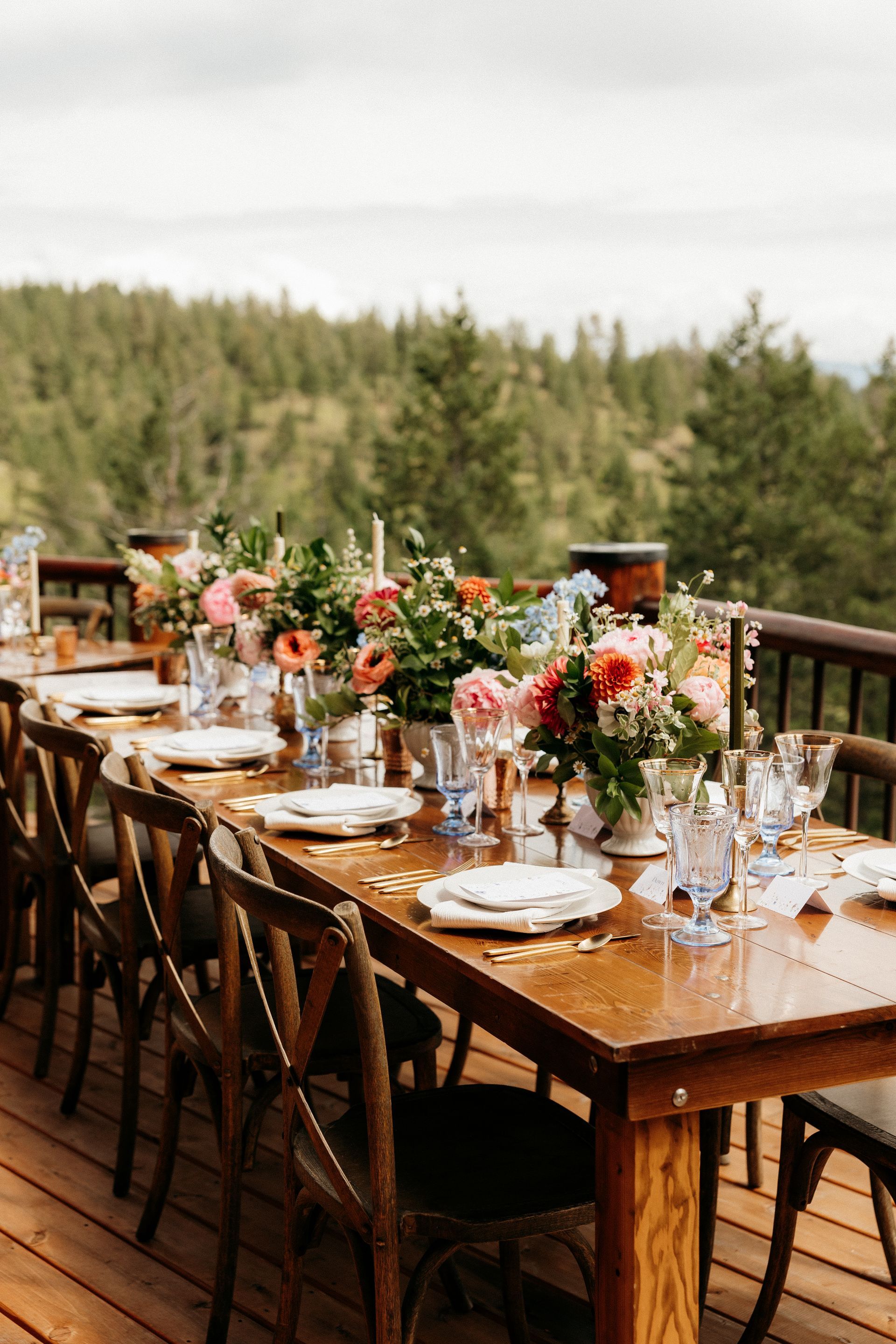A long wooden table with plates , glasses , and flowers on it on a deck.