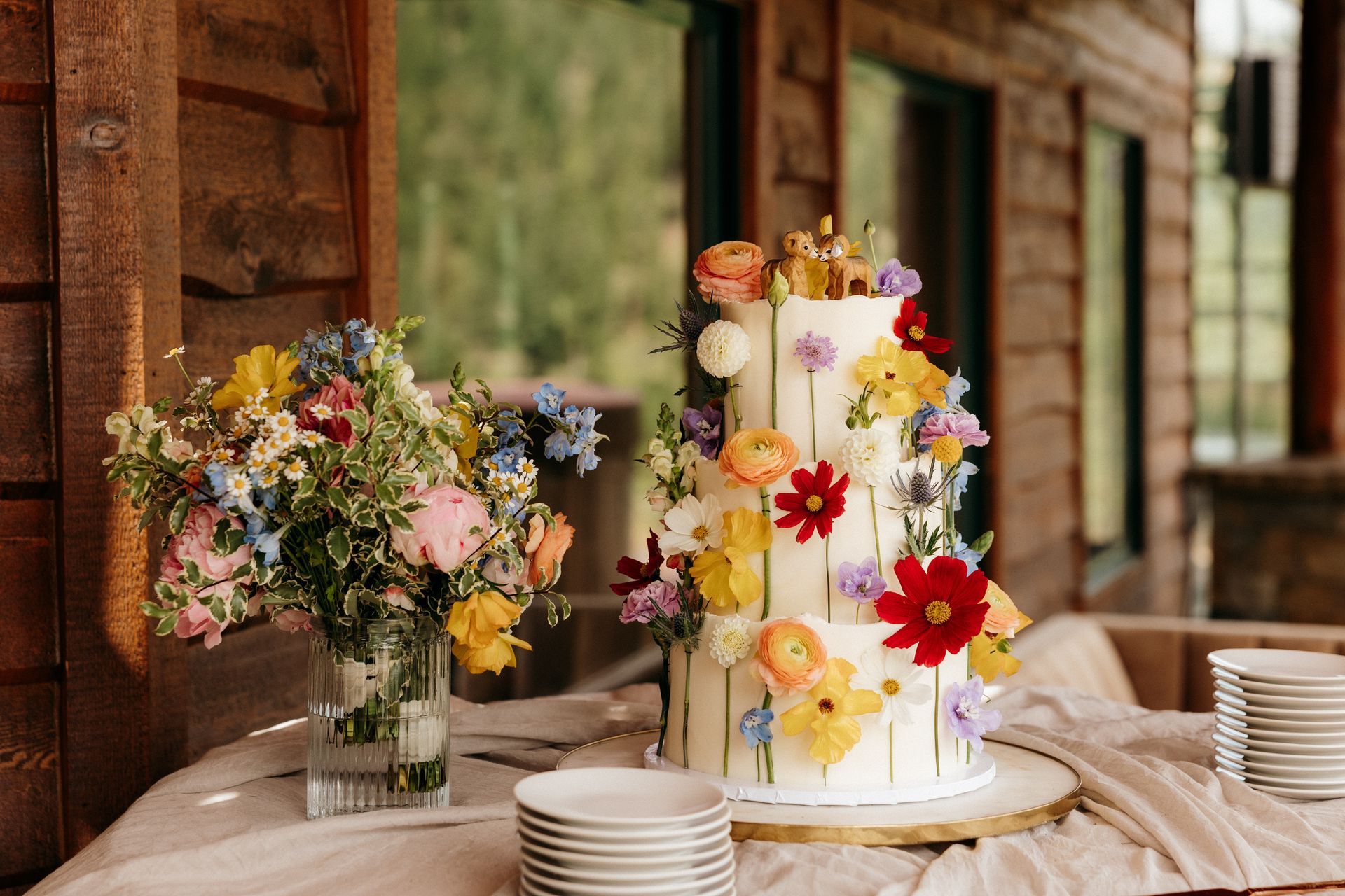A wedding cake with flowers on it is sitting on a table next to a vase of flowers.