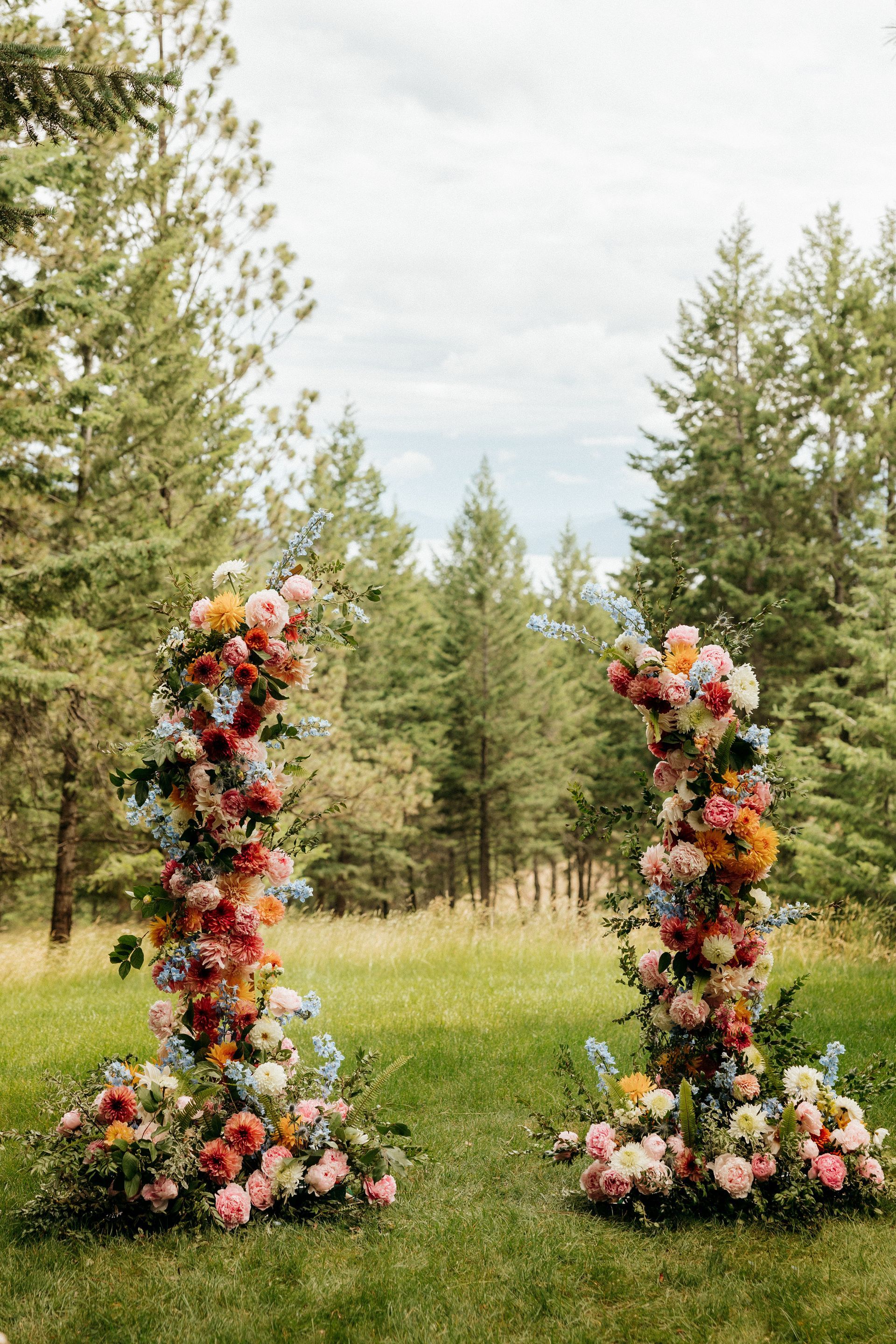 A couple of arches filled with flowers in a field with trees in the background.