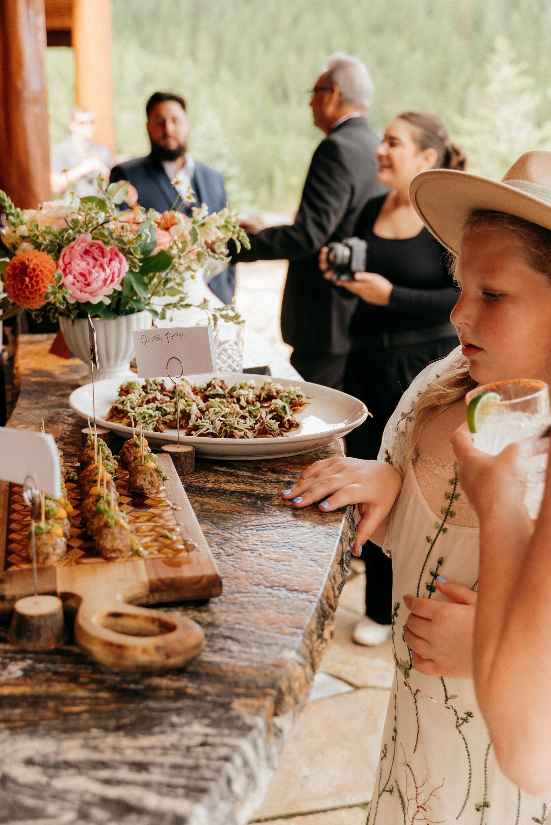 A little girl is standing in front of a buffet table holding a drink.
