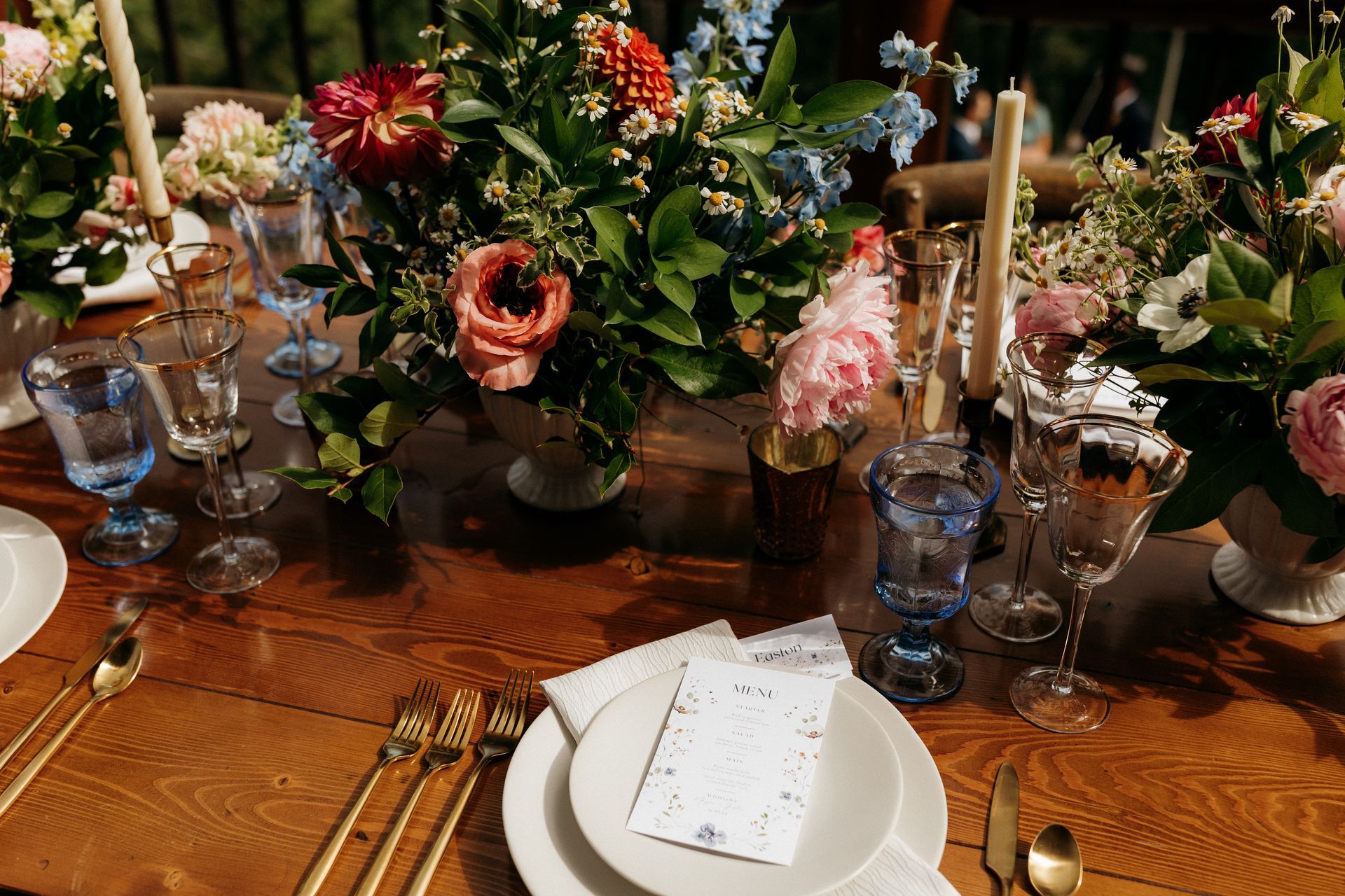 A wooden table with plates , silverware , candles and flowers on it.