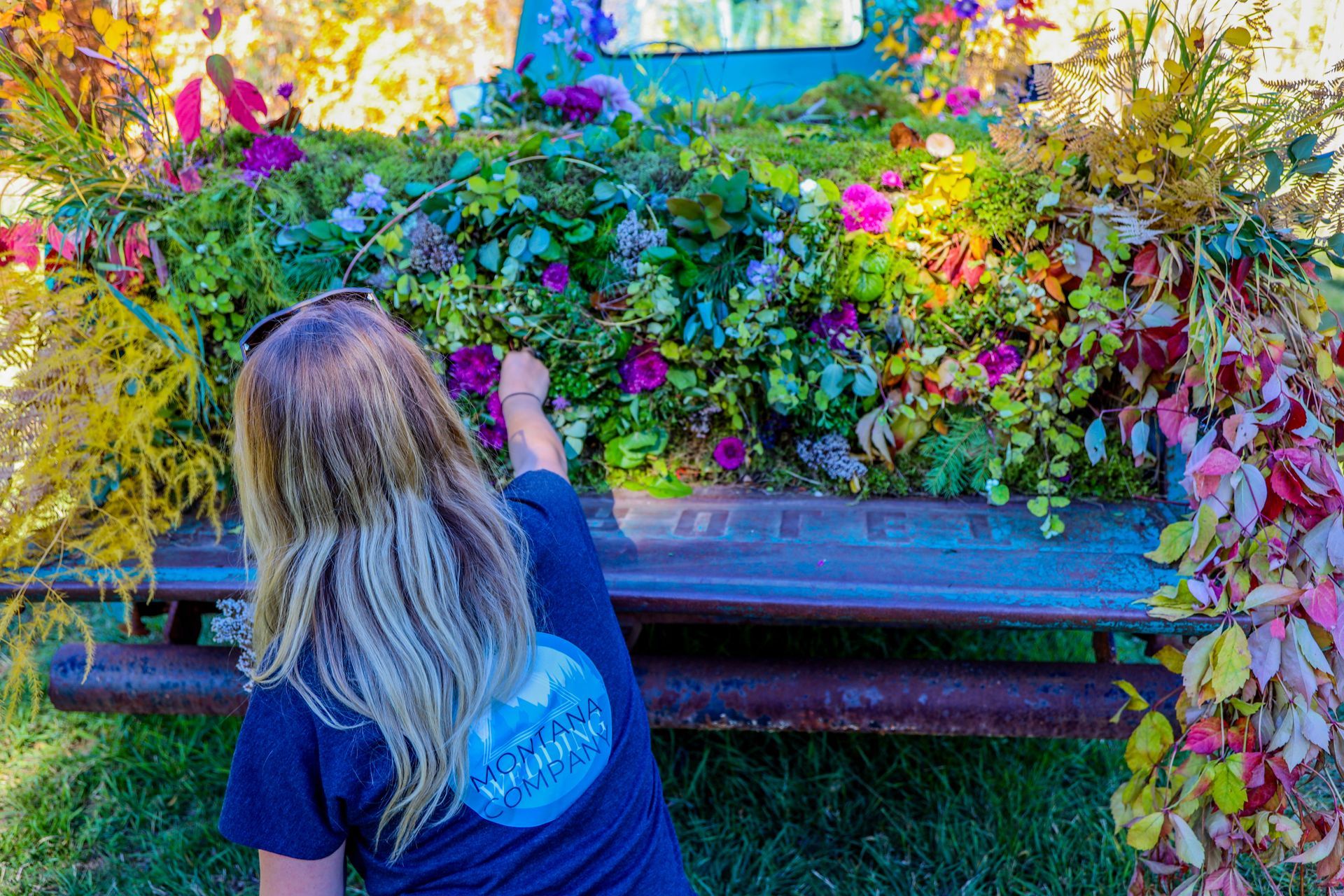 A woman is kneeling down in front of a truck filled with flowers.